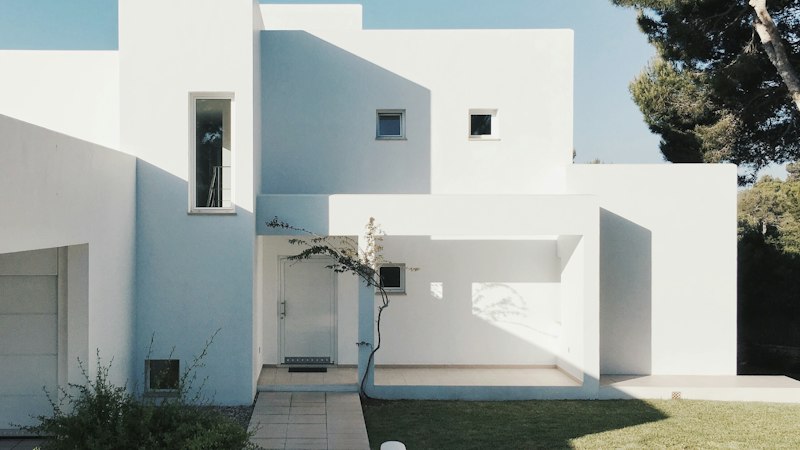 Modern white two-story home with a green front lawn on a sunny day